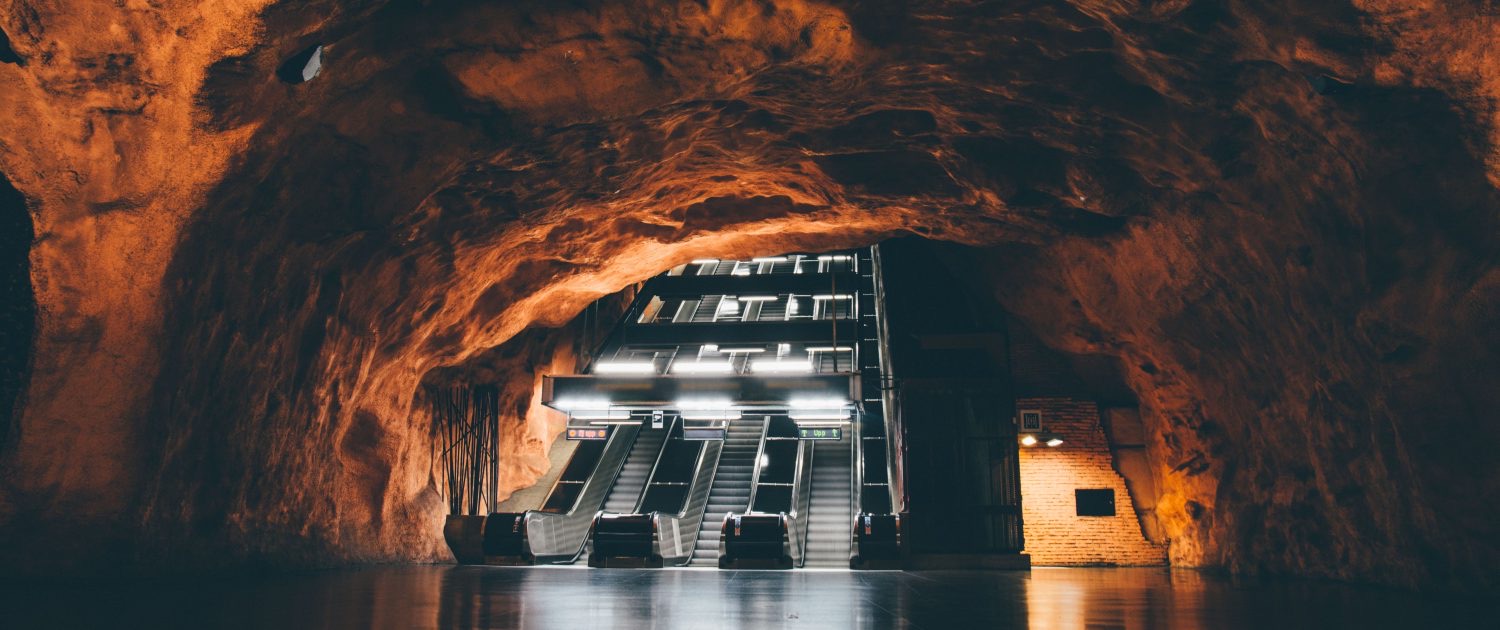 Rulltrappor som går upp genom en tunnelbanestation uthuggen i orangerött berg i Stockholm.